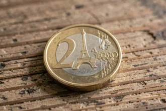 Pièce de 2 euros commémorative JO 2026 avec motif Tour Eiffel et anneaux olympiques posée sur bois vintage